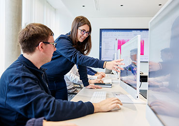 Mitarbeiterin erklärt anderer Person etwas an einem Monitor