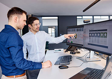 Zwei Mitarbeiter unterhalten sich vor Bildschirm